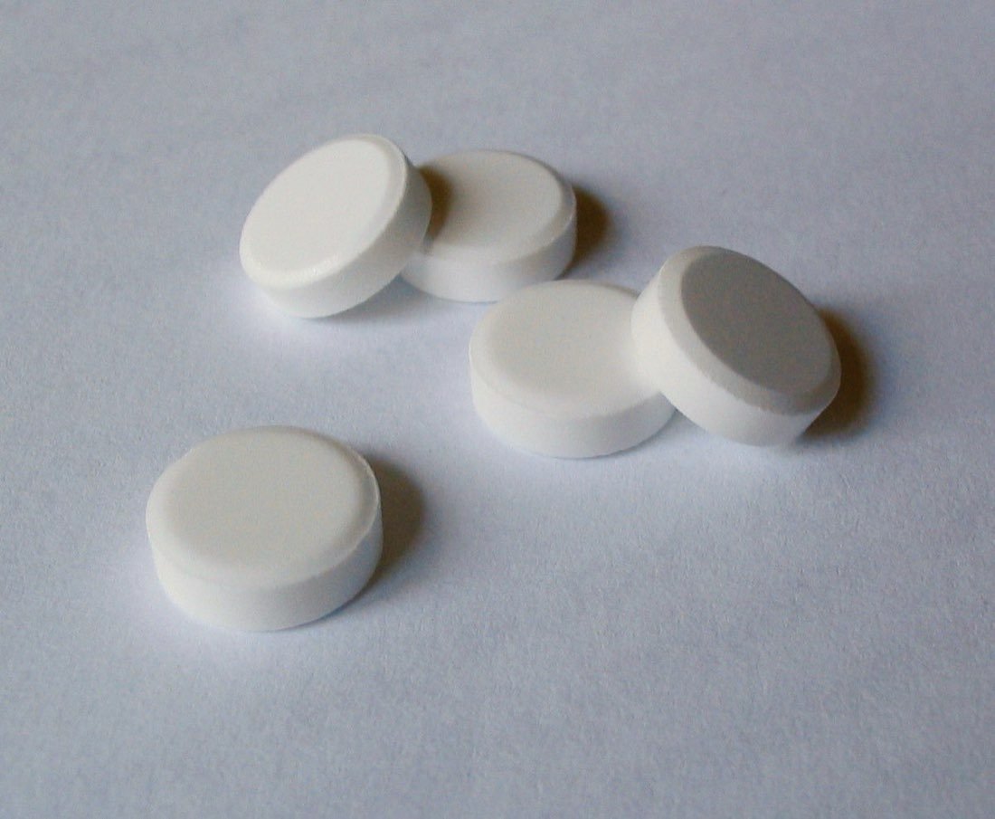 Small white biochemic tissue salt tablets spilling from a glass bottle onto a wooden surface